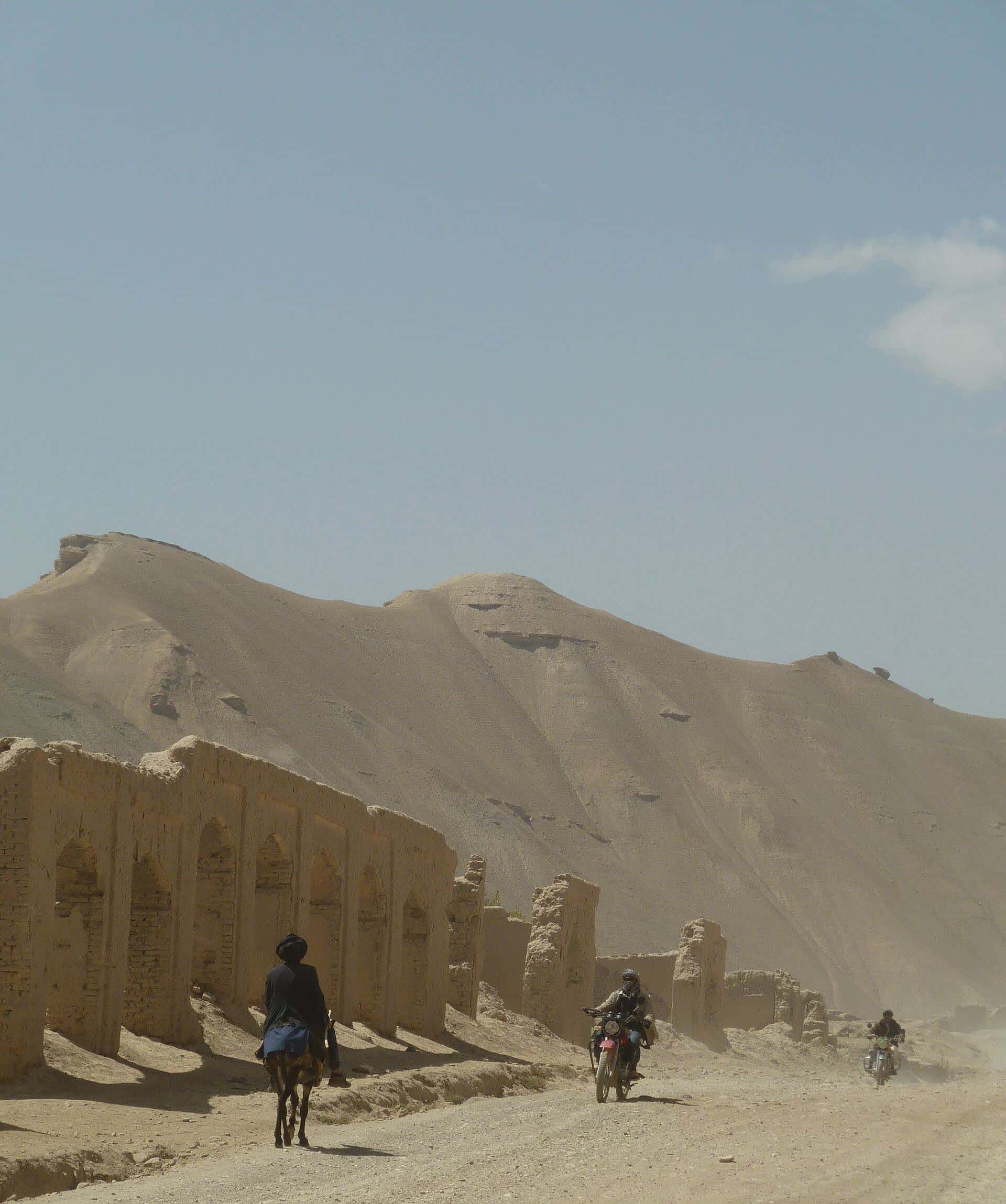 People walking on a dusty road below the cliffs of Bamyan