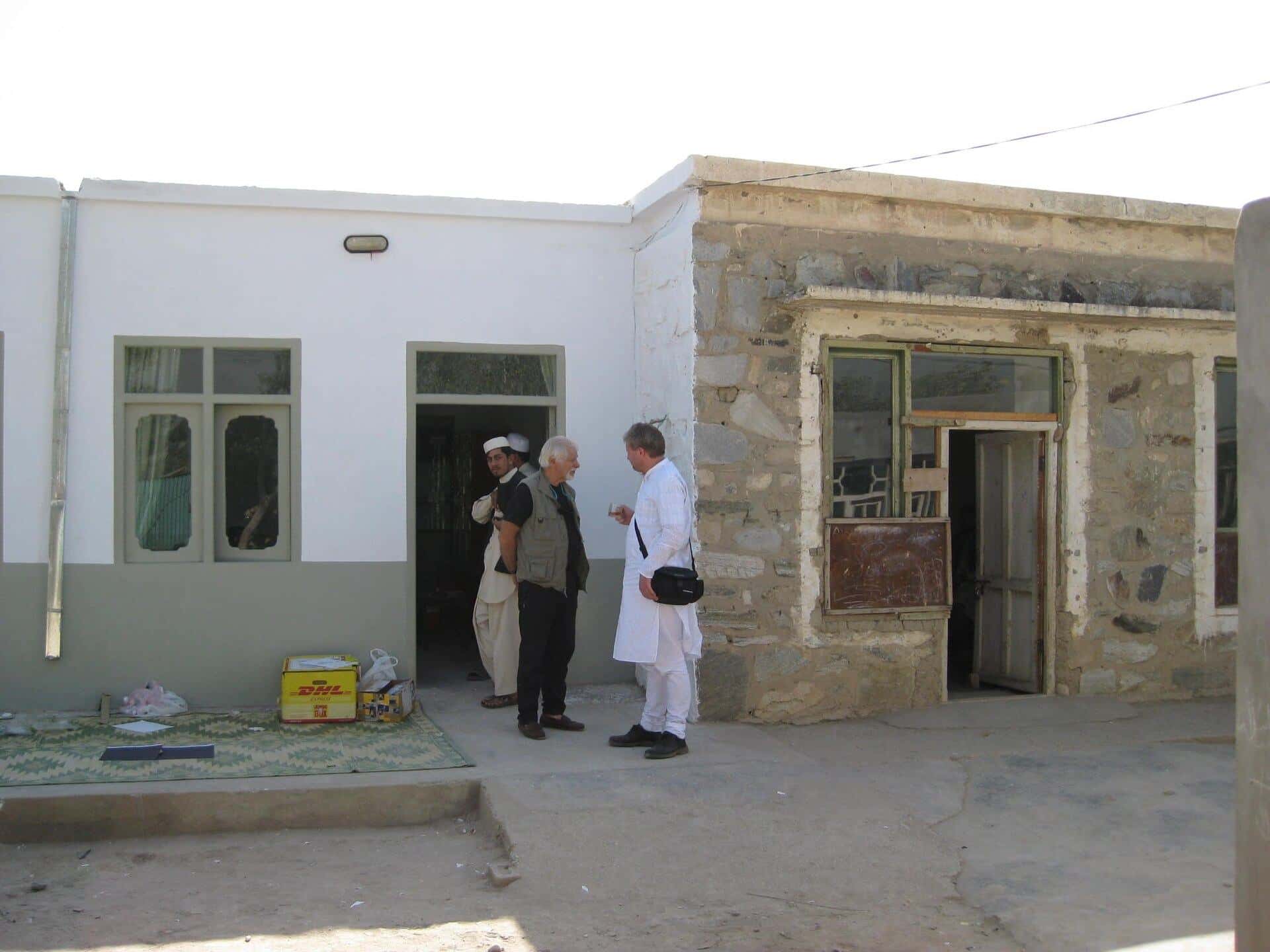 A single-storey white building with men standing at the entrance