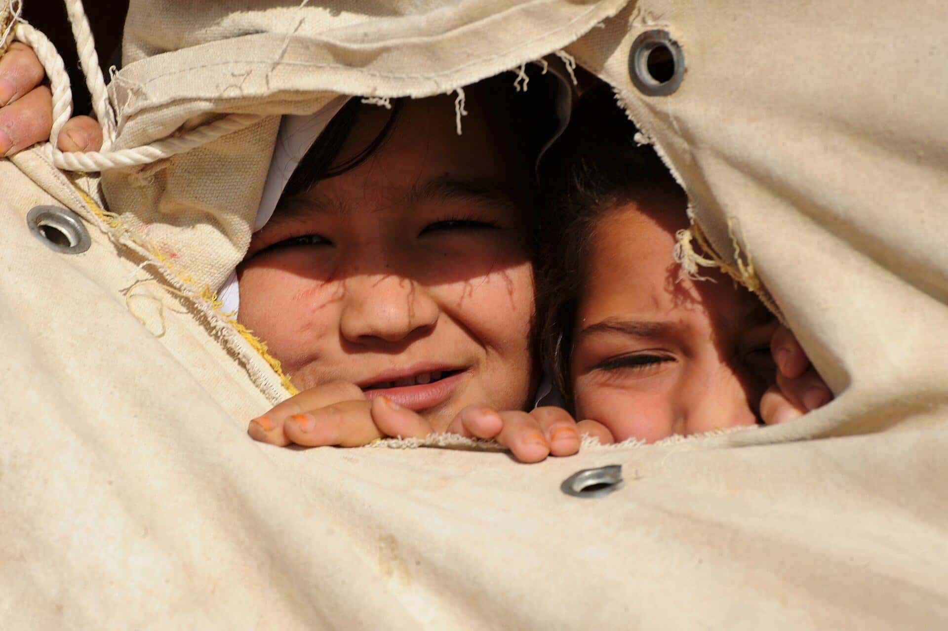 Two young girls peek through an opening in a tent used as a classroom